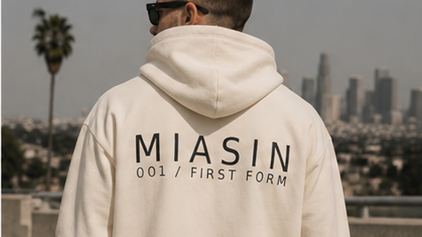 A model photographed from behind wearing the bone MIASIN 001 hoodie against the Los Angeles skyline