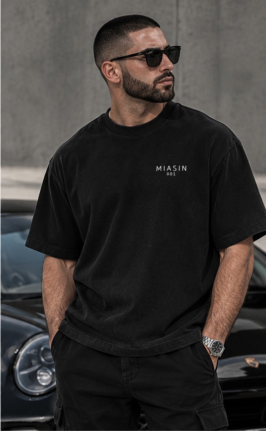 A model wearing the black MIASIN 001 Box Tee and shorts beside a black car