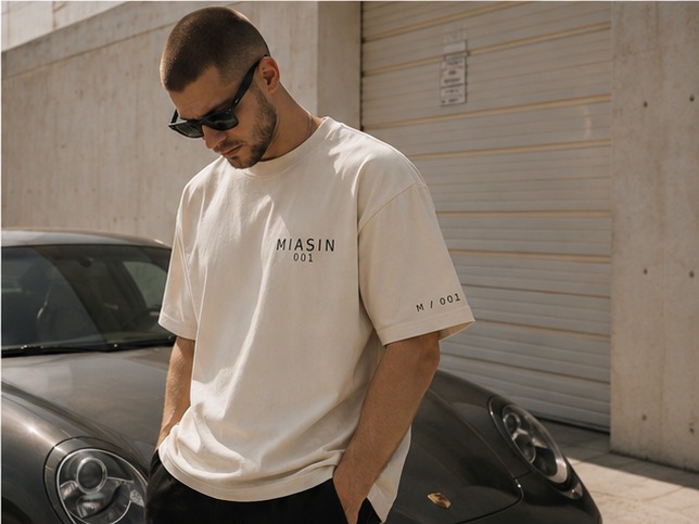 A model in the bone MIASIN 001 Box Tee looking down beside a parked car